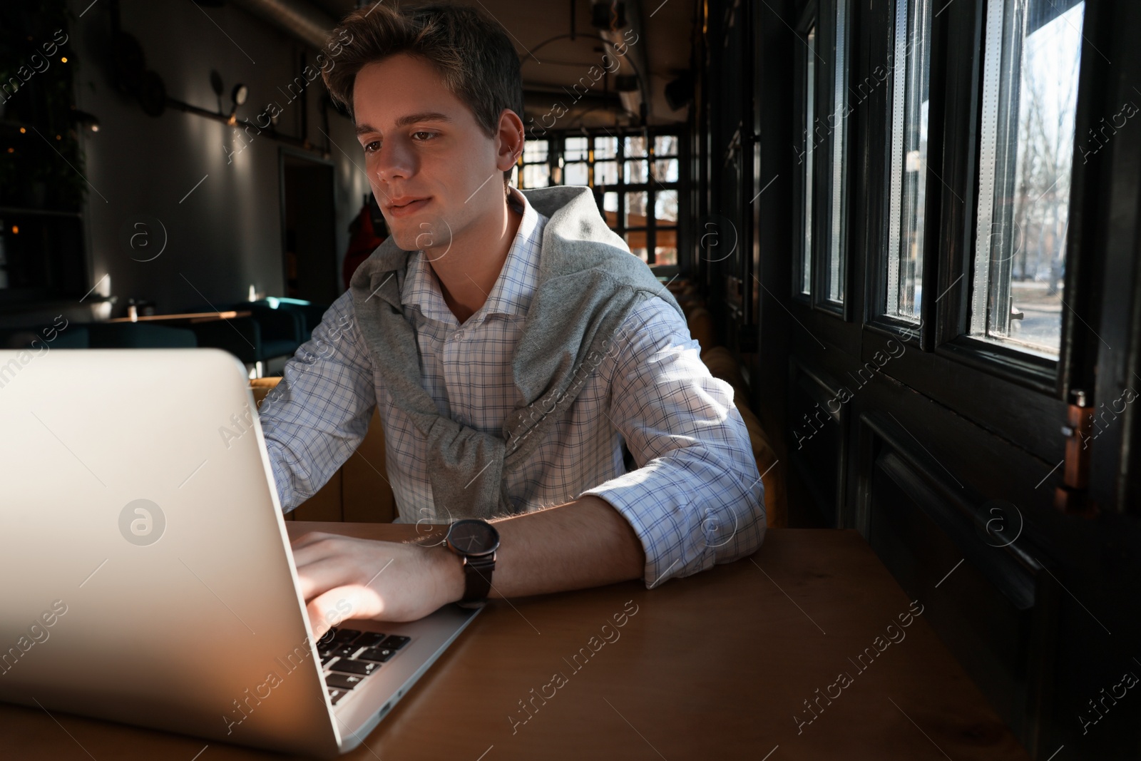 Photo of Teenage student with laptop studying at table in cafe