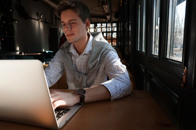 Photo of Teenage student with laptop studying at table in cafe