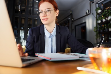 Photo of Young female student with laptop studying at table in cafe