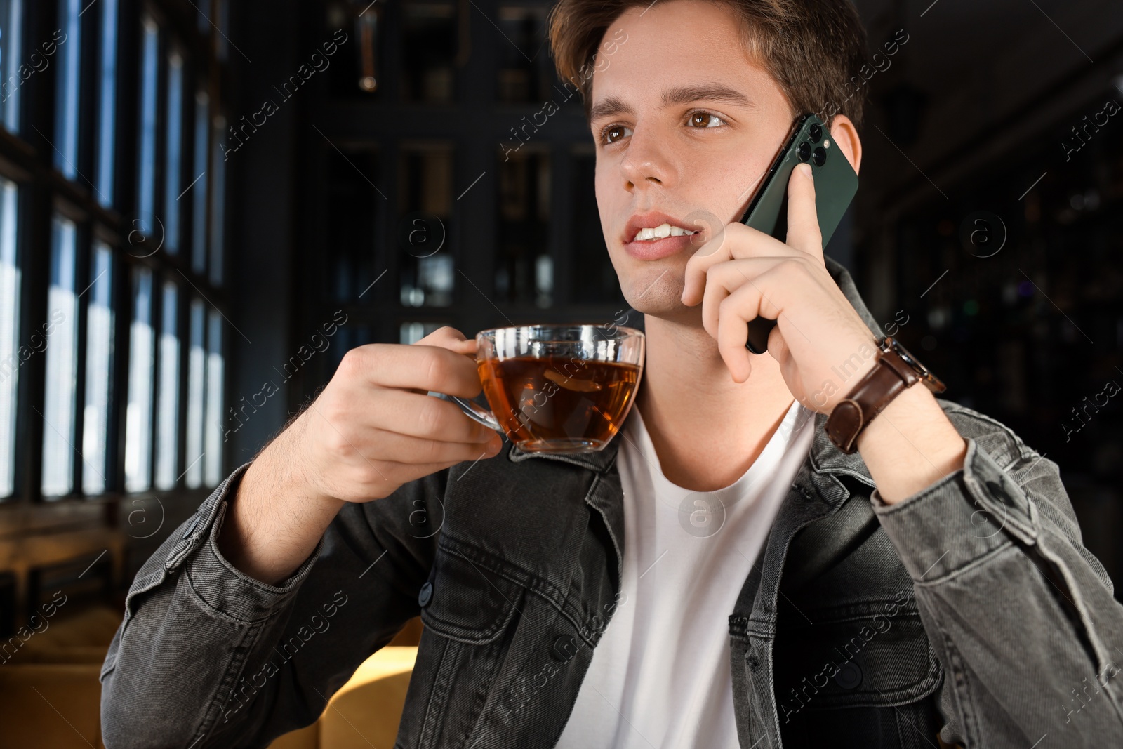 Photo of Teenage boy with cup of tea talking on phone in cafe