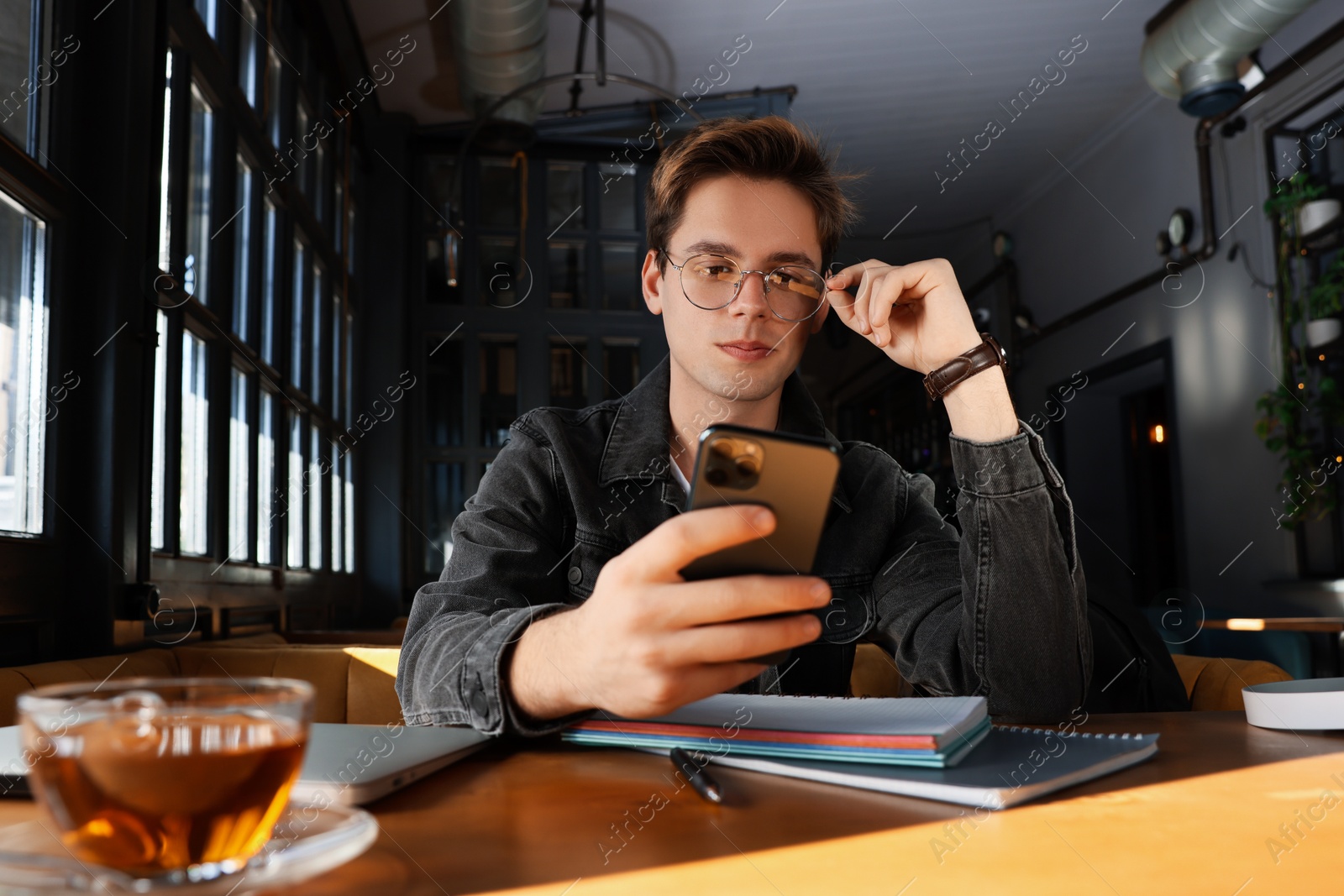 Photo of Teenage student using smartphone while studying at table in cafe
