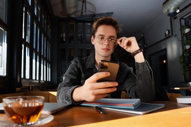 Teenage student using smartphone while studying at table in cafe