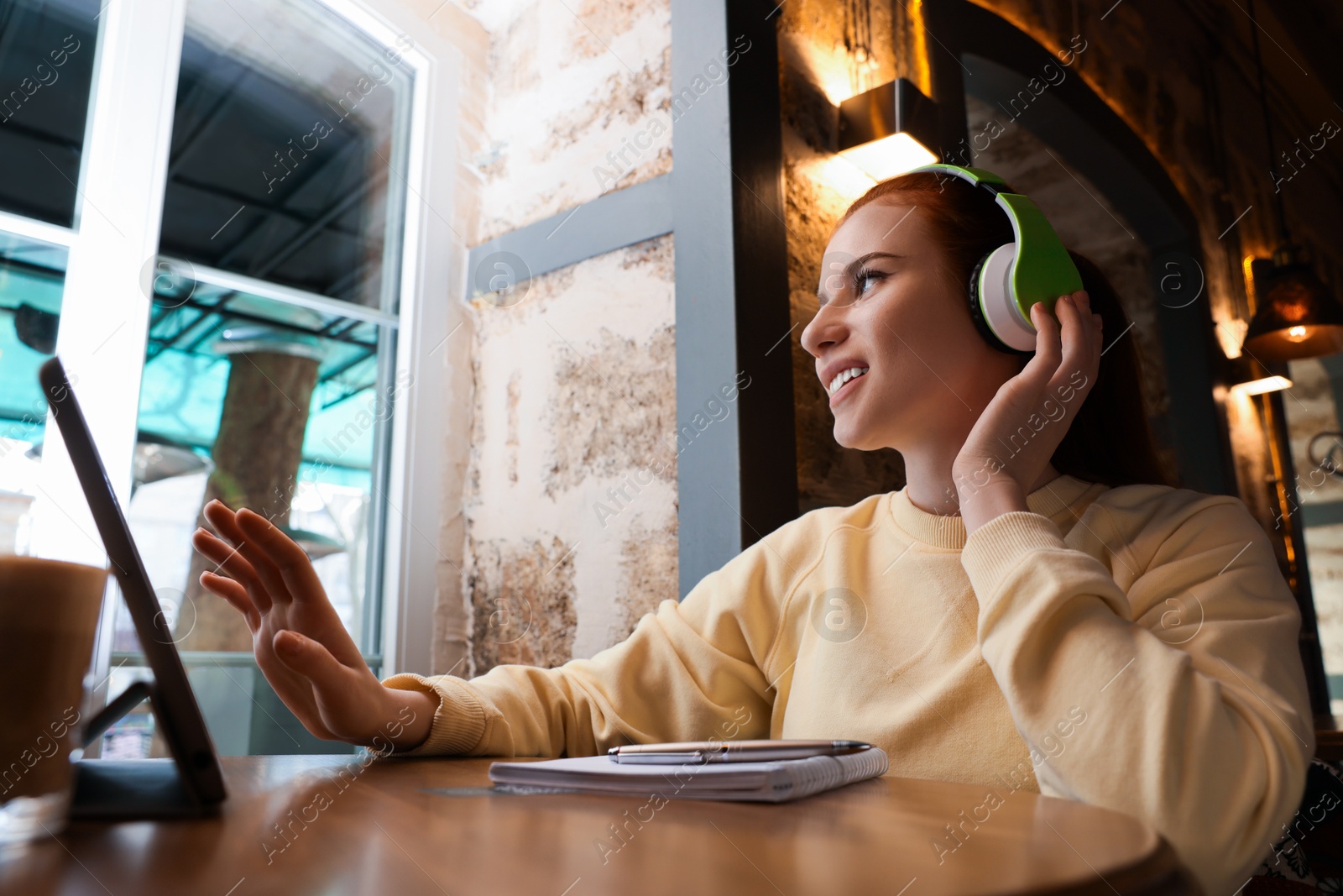 Photo of Young female student with tablet and headphones studying at table in cafe, low angle view