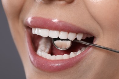 Examining woman's teeth with dentist's mirror on grey background, closeup