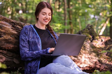 Smiling freelancer working with laptop in forest, low angle view. Remote job