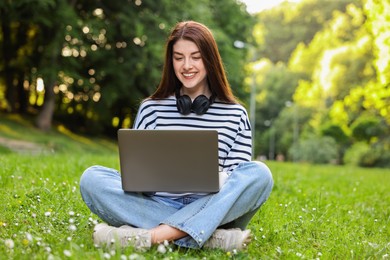 Smiling freelancer working with laptop on green grass outdoors. Remote job