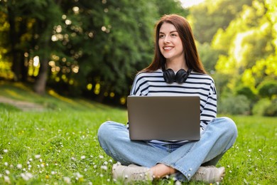 Smiling freelancer working with laptop on green grass outdoors, space for text. Remote job