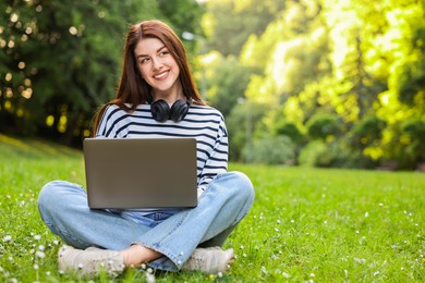 Smiling freelancer working with laptop on green grass outdoors, space for text. Remote job