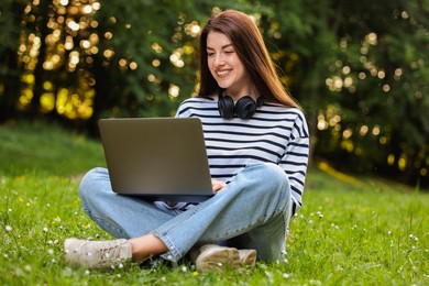 Smiling freelancer working with laptop on green grass outdoors. Remote job