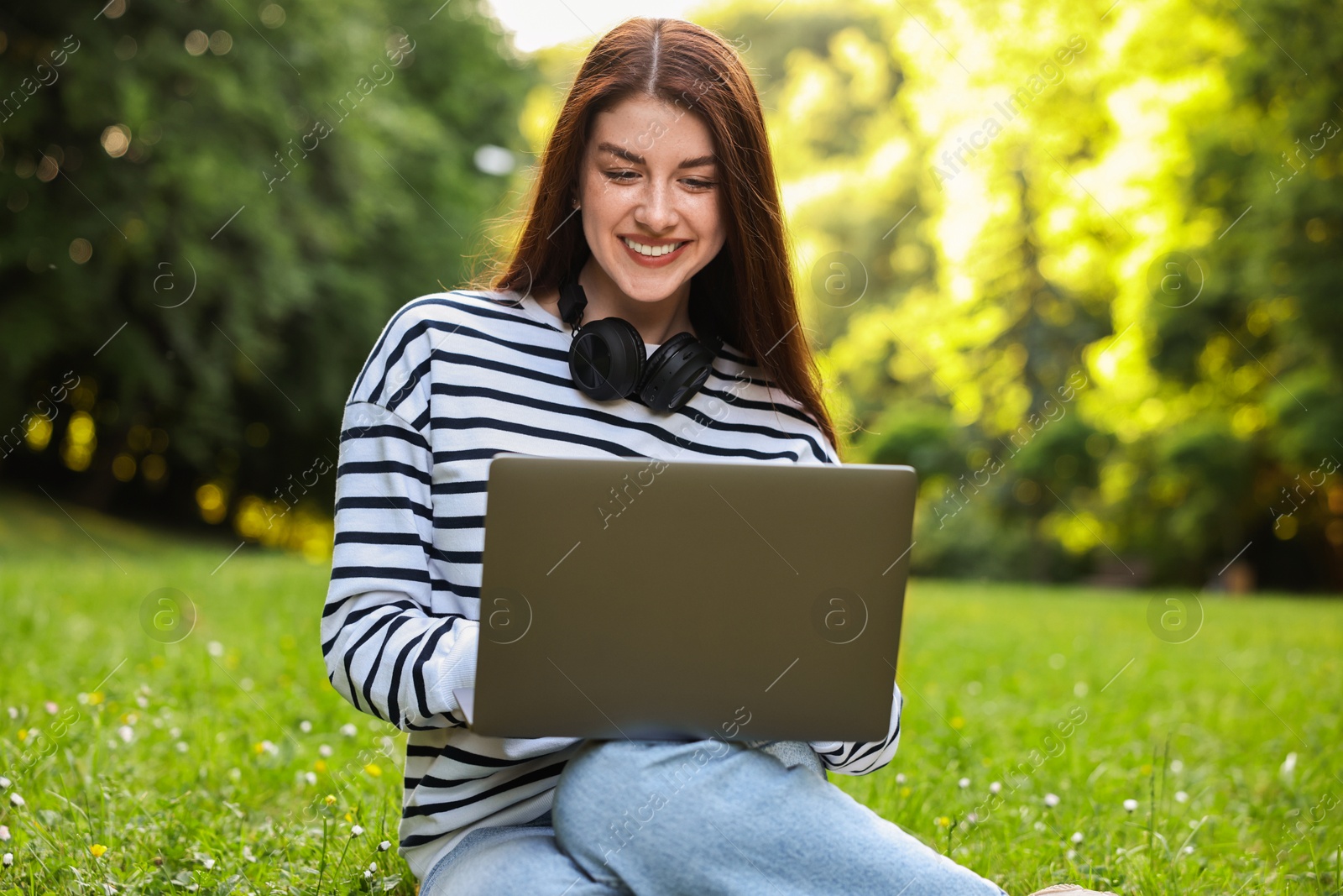 Photo of Smiling freelancer working with laptop on green grass outdoors. Remote job