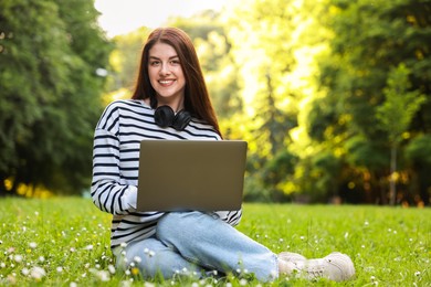 Smiling freelancer working with laptop on green grass outdoors, space for text. Remote job