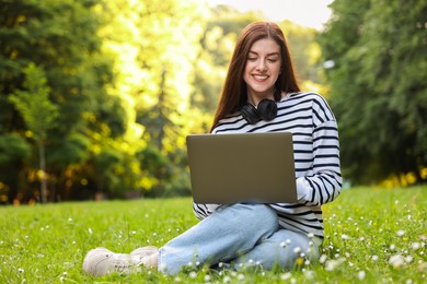 Smiling freelancer working with laptop on green grass outdoors, space for text. Remote job