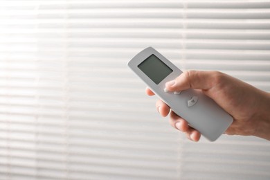 Man using remote control to adjust window blinds indoors, closeup. Space for text