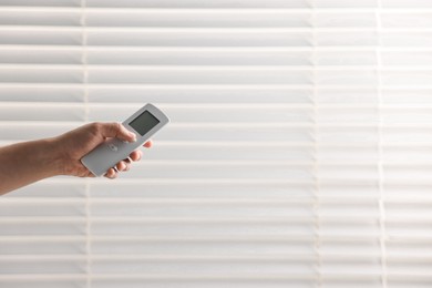 Photo of Man using remote control to adjust window blinds indoors, closeup. Space for text