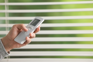 Photo of Man using remote control to adjust window blinds indoors, closeup. Space for text