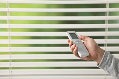 Photo of Man using remote control to adjust window blinds indoors, closeup. Space for text