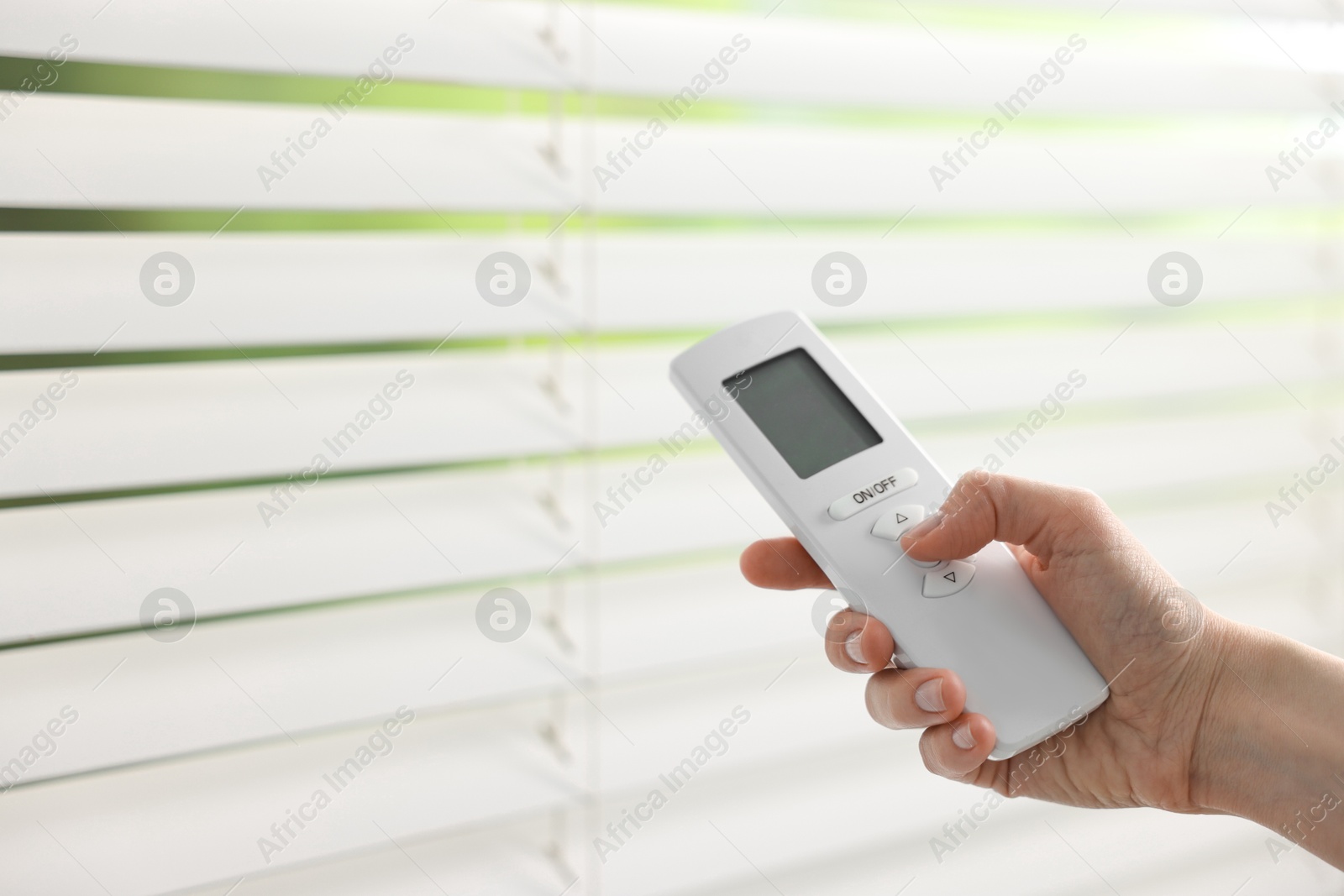 Photo of Woman using remote control to adjust window blinds indoors, closeup. Space for text