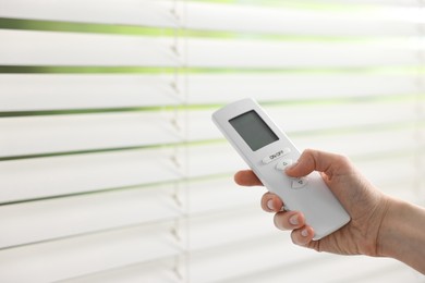 Woman using remote control to adjust window blinds indoors, closeup. Space for text