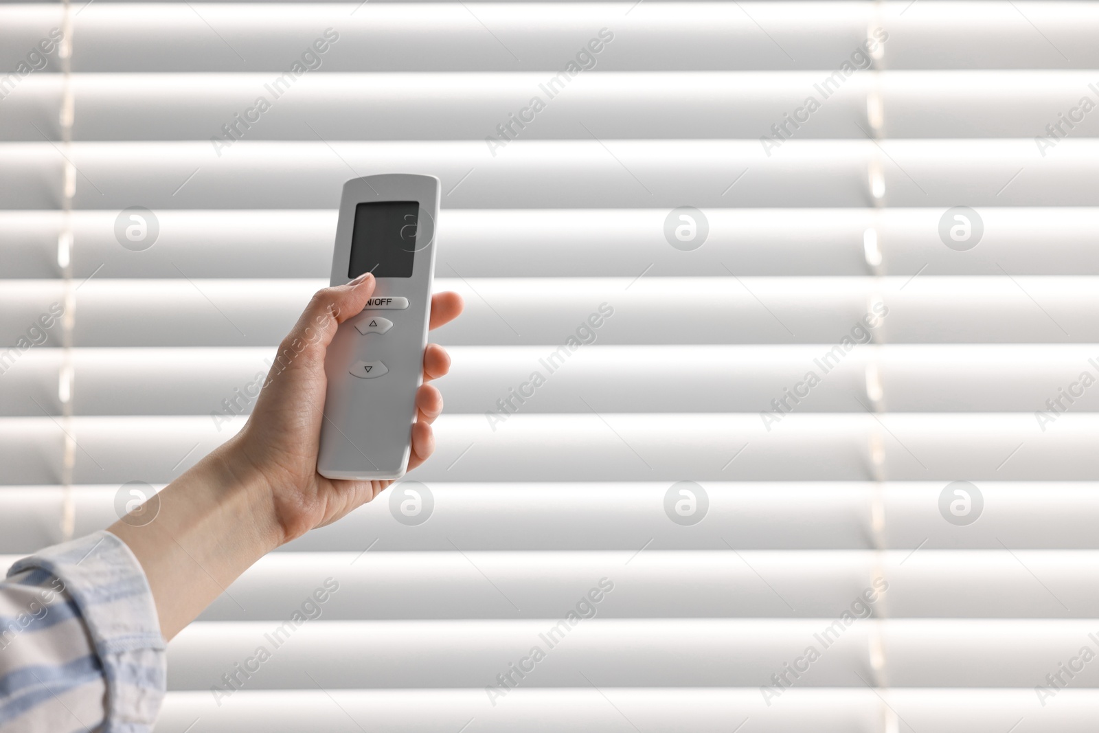 Photo of Woman using remote control to adjust window blinds indoors, closeup. Space for text