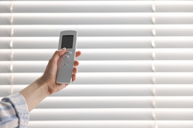 Photo of Woman using remote control to adjust window blinds indoors, closeup. Space for text