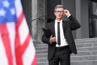 International relations. Diplomat with clipboard near flag of USA outdoors