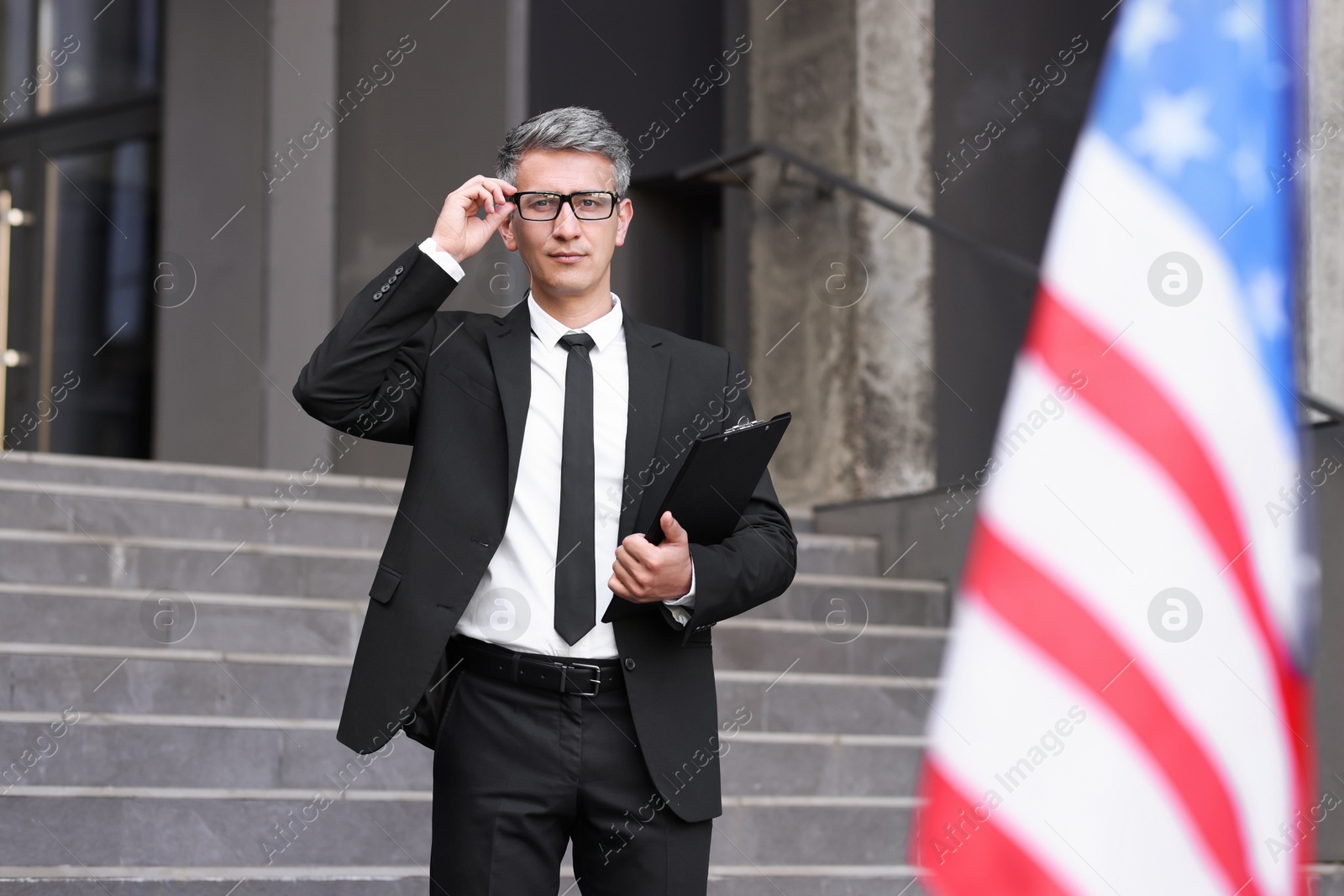 Photo of International relations. Diplomat with clipboard near flag of USA outdoors