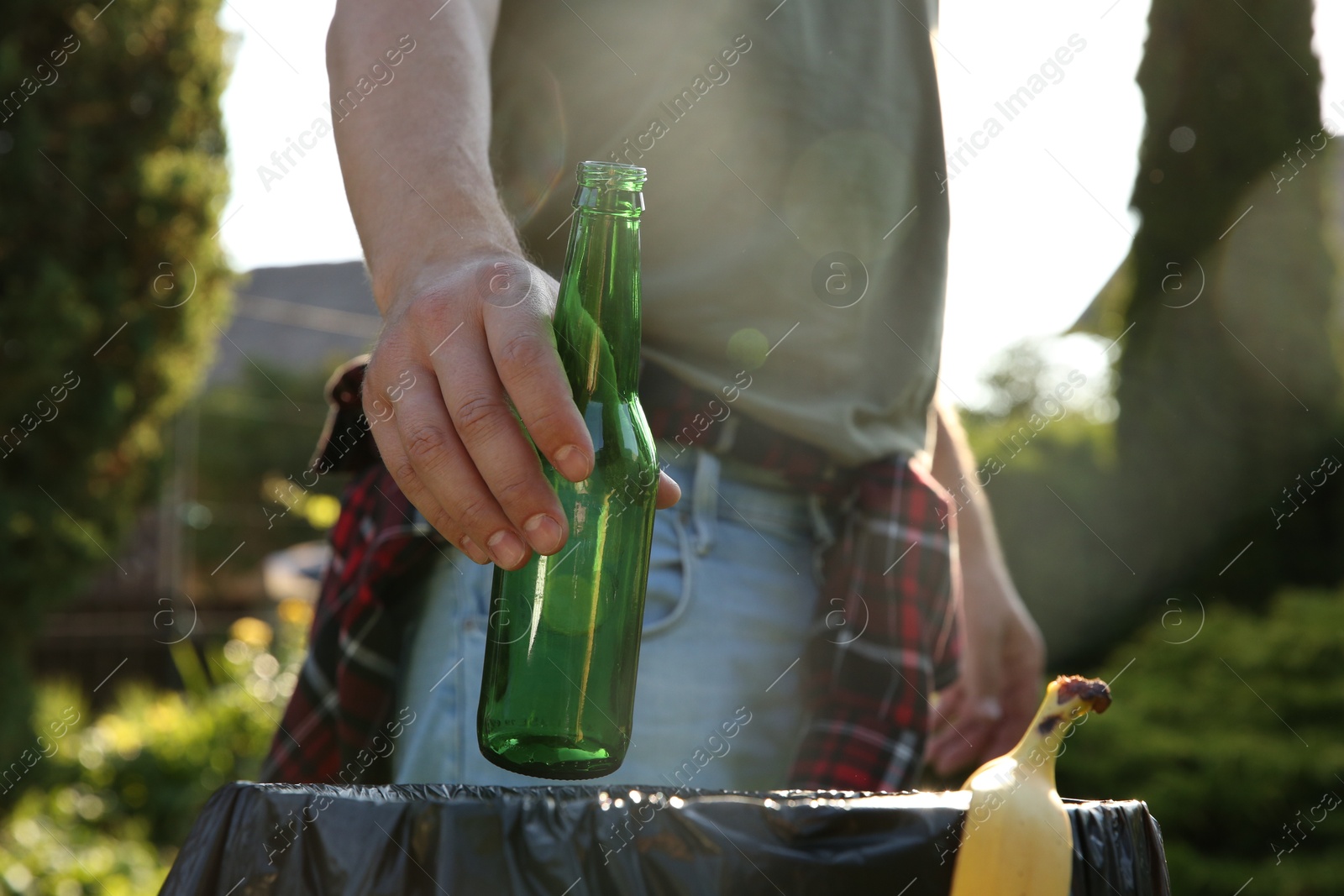 Photo of Man throwing glass bottle into garbage bin outdoors, closeup