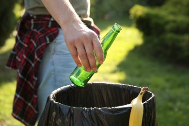 Photo of Man throwing glass bottle into garbage bin outdoors, closeup