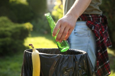 Photo of Man throwing glass bottle into garbage bin outdoors, closeup