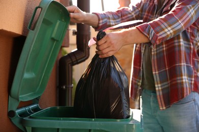 Photo of Man throwing trash bag full of garbage into bin outdoors, closeup