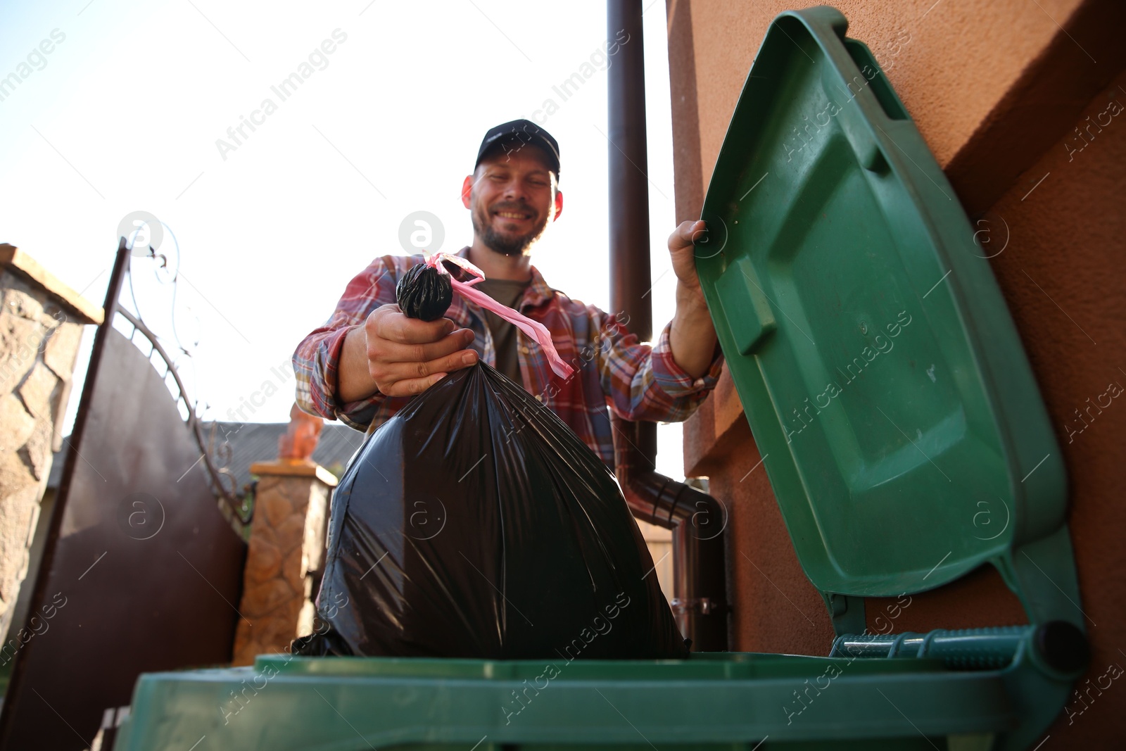 Photo of Man throwing trash bag full of garbage into bin outdoors, low angle view