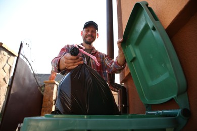Man throwing trash bag full of garbage into bin outdoors, low angle view