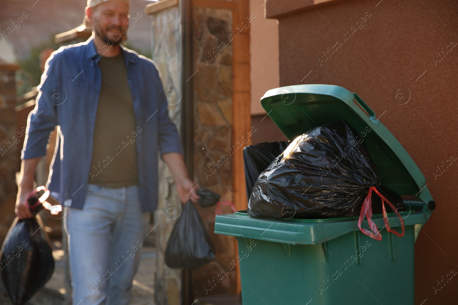 Photo of Man with trash bags full of garbage and bin outdoors, selective focus