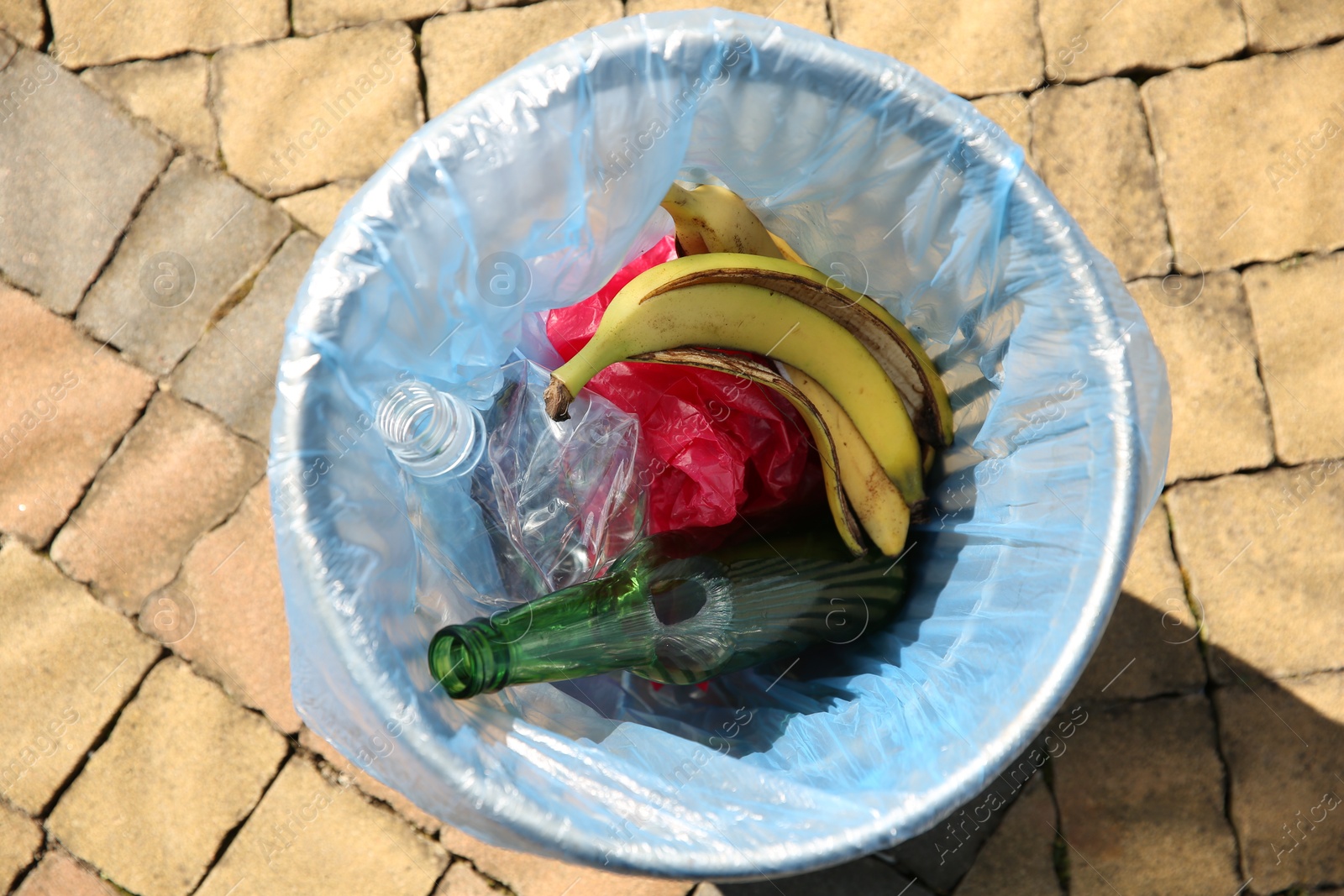 Photo of Trash bag with garbage in bin outdoors, top view