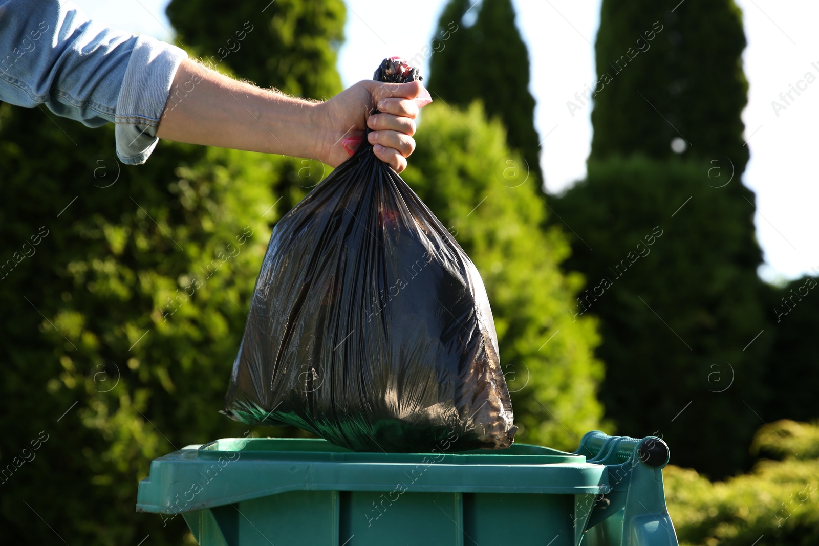 Photo of Man throwing trash bag into bin outdoors, closeup