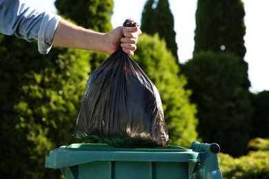Photo of Man throwing trash bag into bin outdoors, closeup