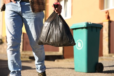 Photo of Man with trash bag full of garbage and bin outdoors, closeup