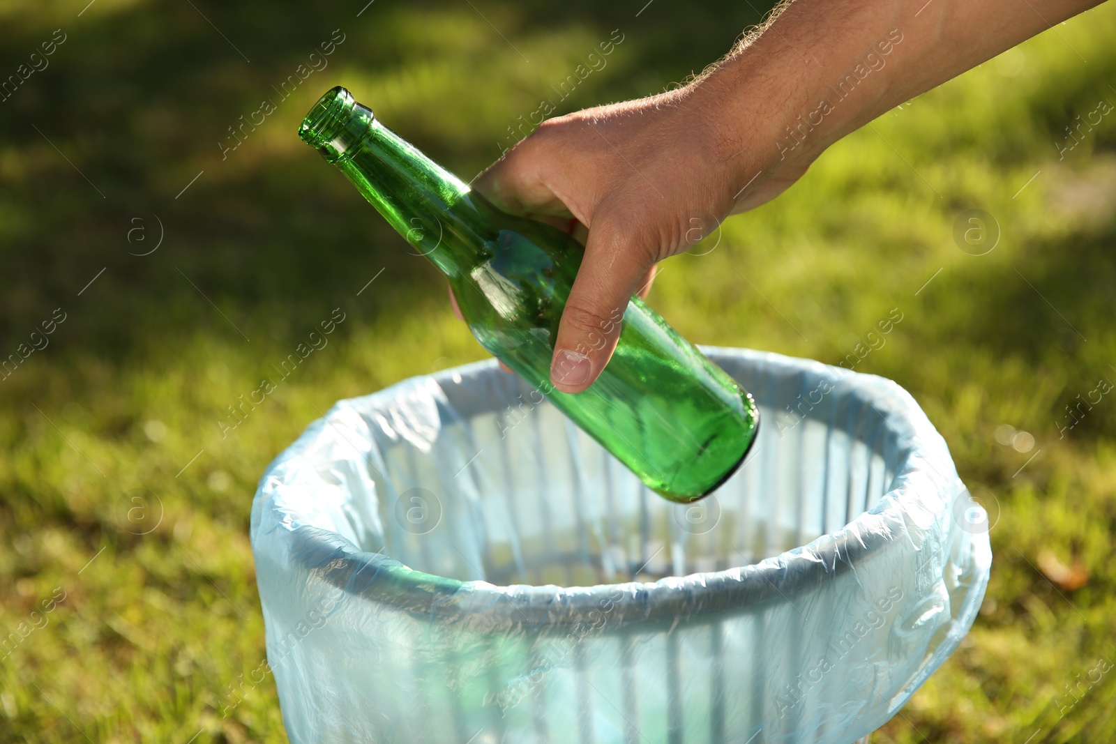 Photo of Man throwing glass bottle into garbage bin outdoors, closeup