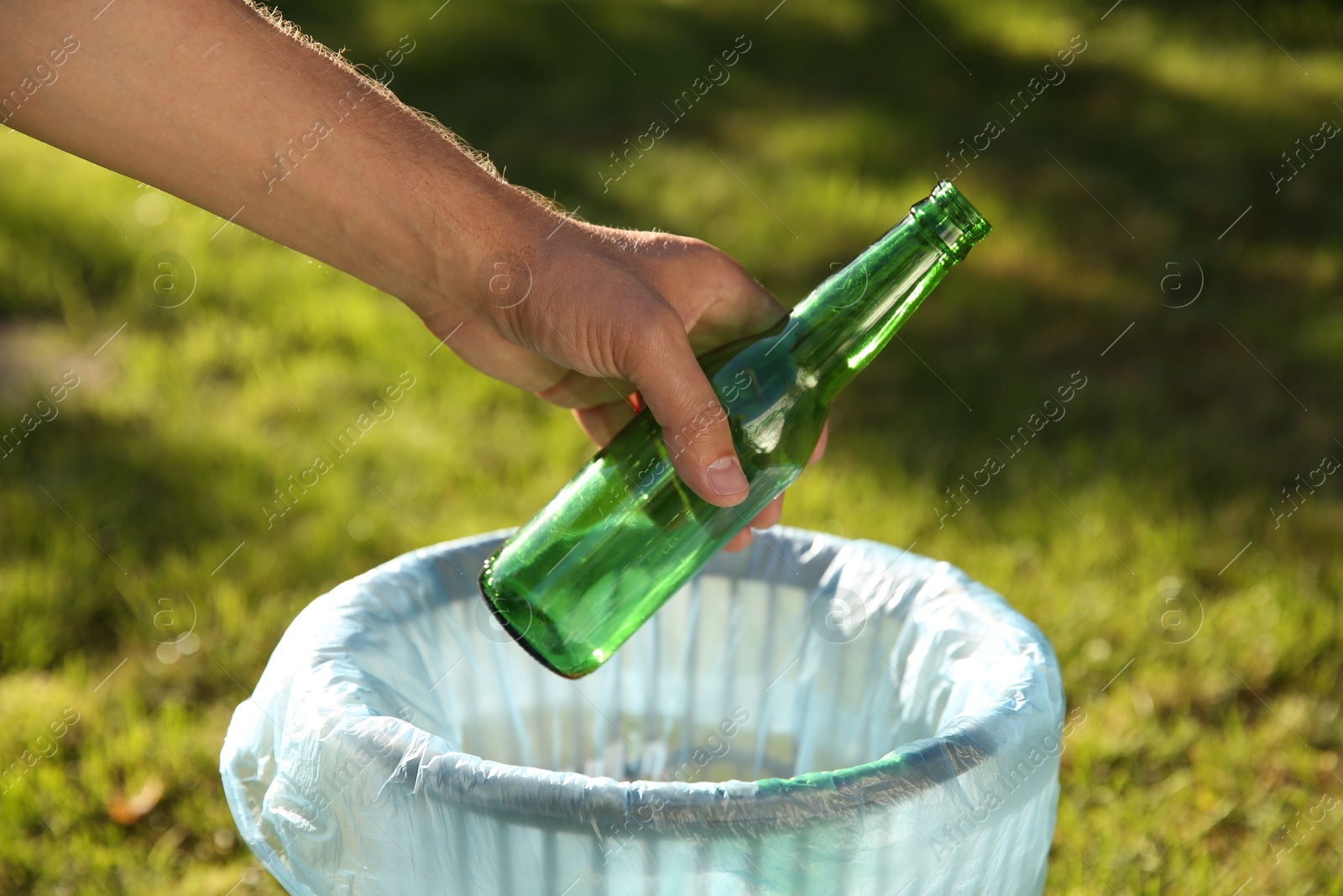 Photo of Man throwing glass bottle into garbage bin outdoors, closeup