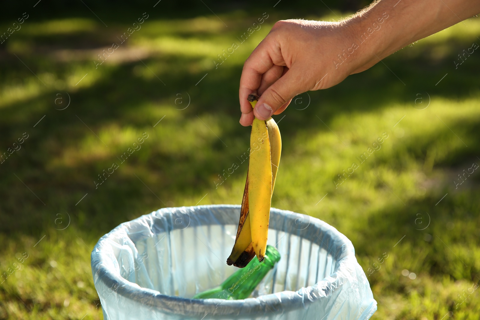 Photo of Man throwing banana peel into garbage bin outdoors, closeup