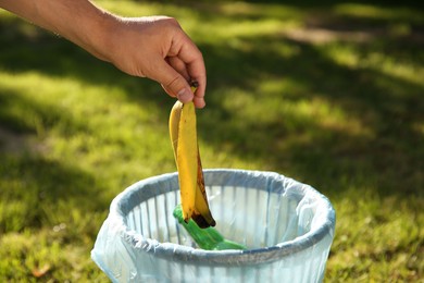 Photo of Man throwing banana peel into garbage bin outdoors, closeup