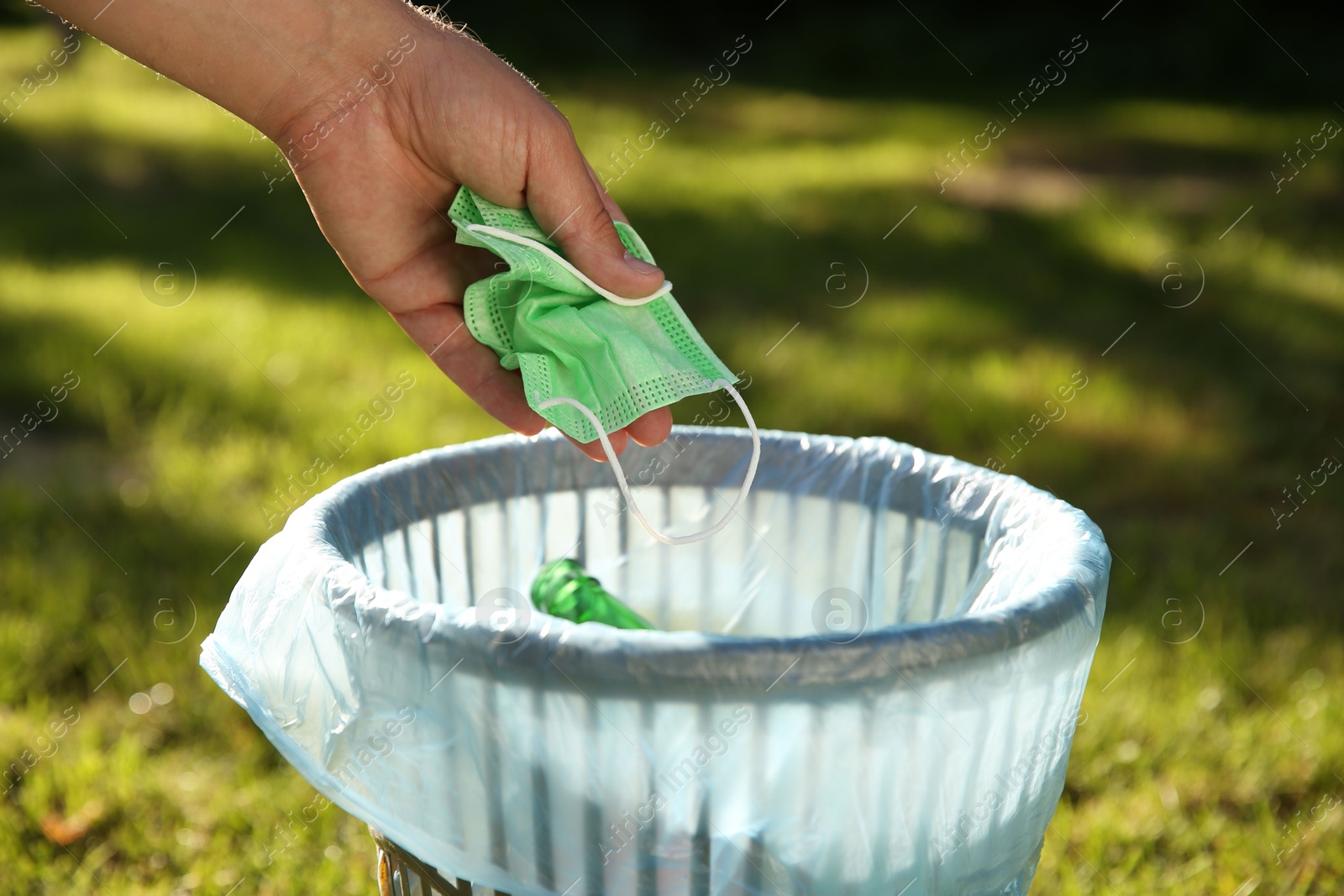 Photo of Man throwing medical mask into garbage bin outdoors, closeup