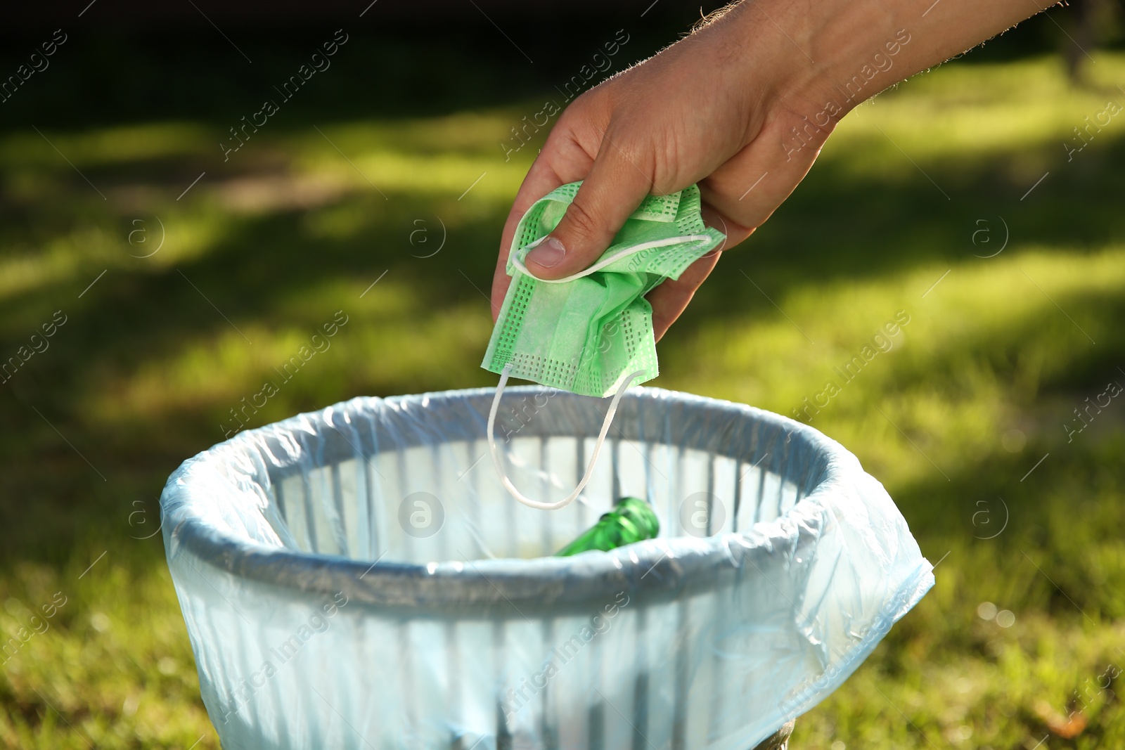 Photo of Man throwing medical mask into garbage bin outdoors, closeup