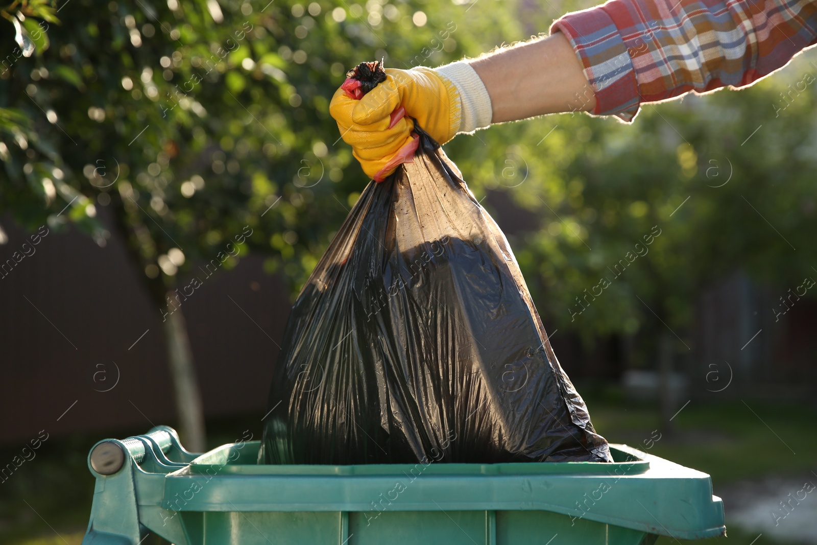 Photo of Man throwing trash bag into bin outdoors, closeup