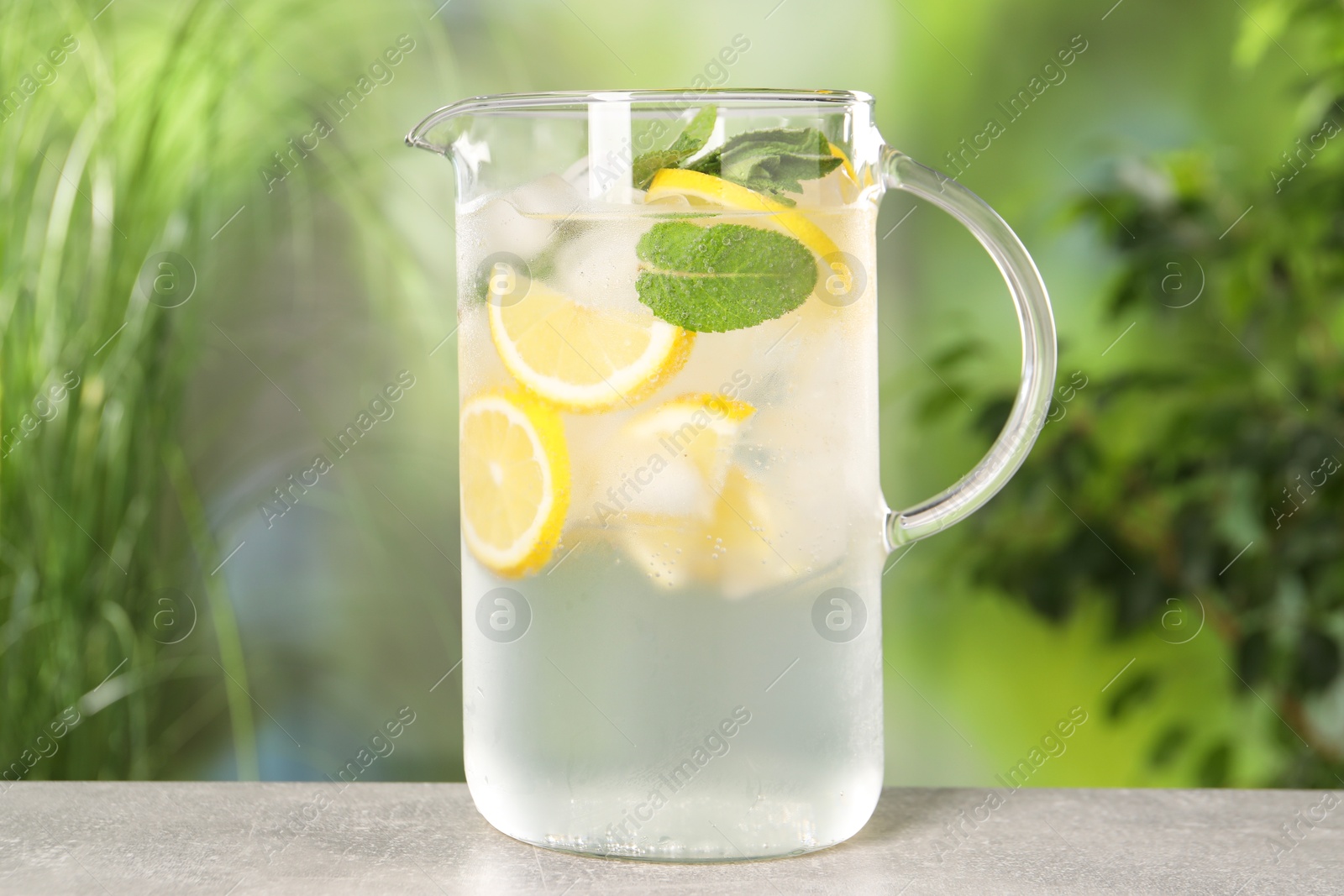 Photo of Freshly made lemonade with mint in jug on grey table outdoors