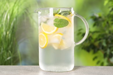 Freshly made lemonade with mint in jug on grey table outdoors