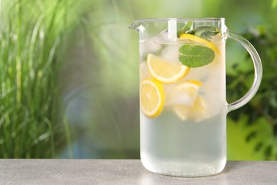 Freshly made lemonade with mint in jug on grey table outdoors, space for text