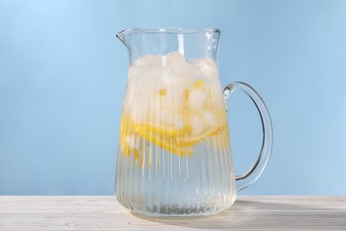 Photo of Freshly made lemonade in jug on white wooden table against light blue background