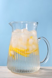 Photo of Freshly made lemonade in jug on white wooden table against light blue background