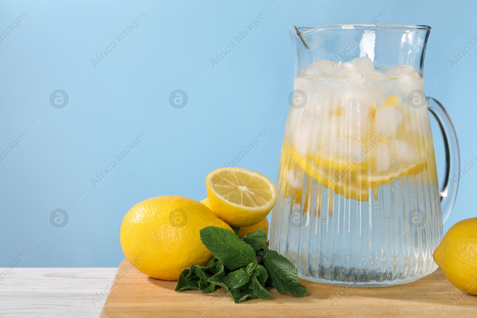 Photo of Freshly made lemonade with mint in jug on white wooden table against light blue background, space for text